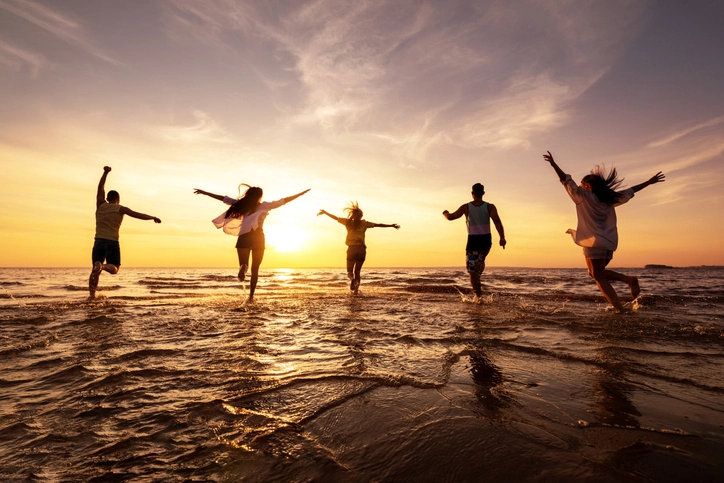 Five friends smiling and running together at sunset on a beach